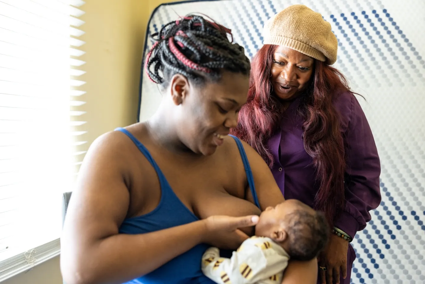 Woman breastfeeds newborn while a doula looks on and guides