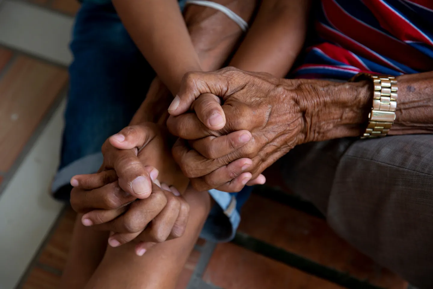 An elderly set of hands holds onto younger hands in this close-up shot.