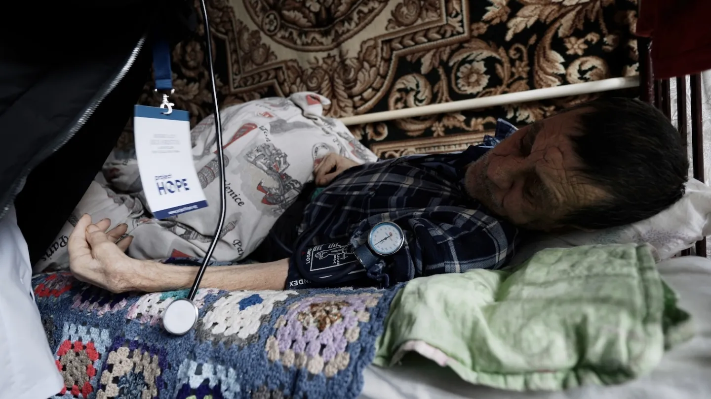 elderly man laying on bed gets his blood pressure checked in Ukraine.