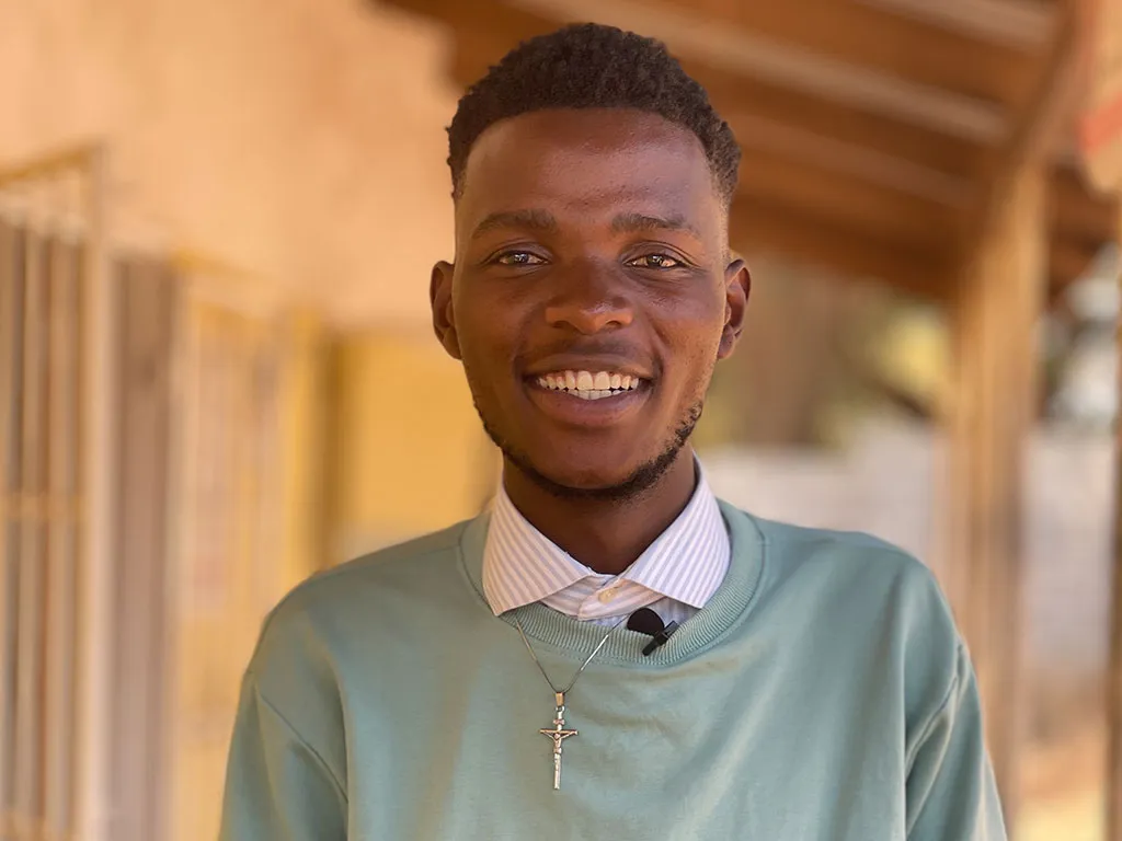 young man in white collared shirt and light blue sweater smiles to camera